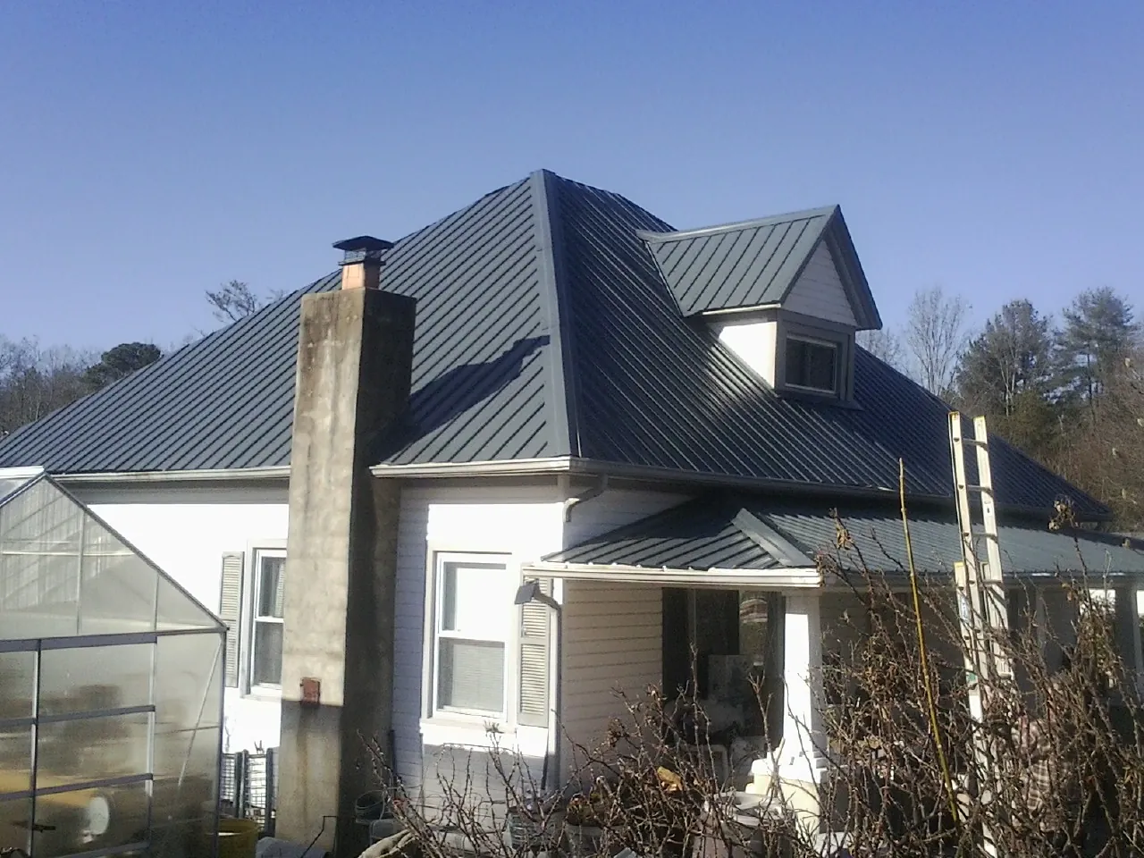 Dark blue standing seam metal roof on a white farmhouse with dormer — Slate & Tile Roof Repair by Roofing Brothers in Bradenville