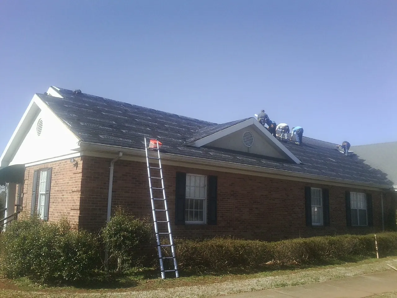 Crew tearing shingles off a brick ranch roof with a ladder set — Emergency Roof Repair work by our crew in Bradenville