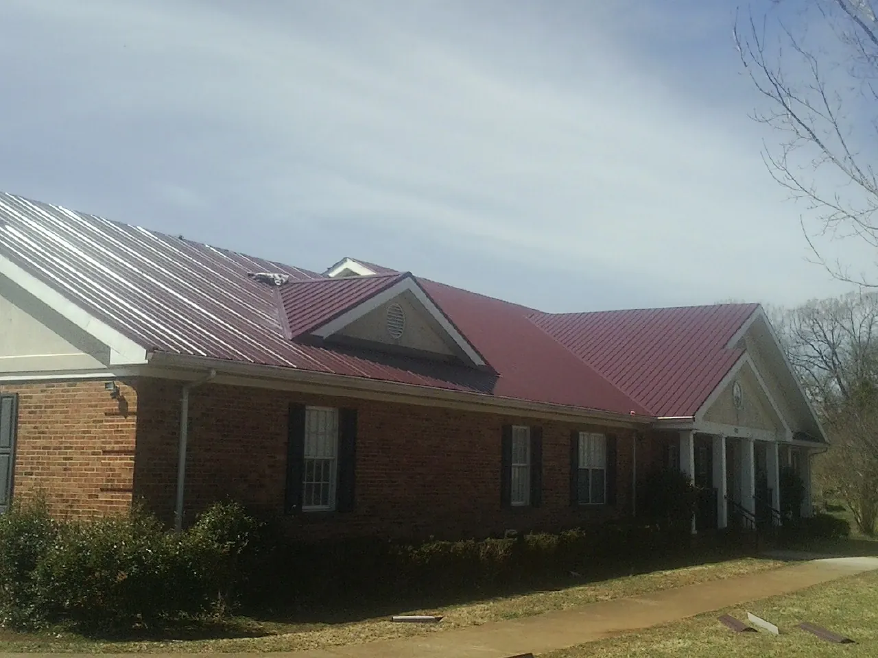 Red metal roof with gabled entries on a long brick building, from a Hail Damage Roof Repair job in Bradenville