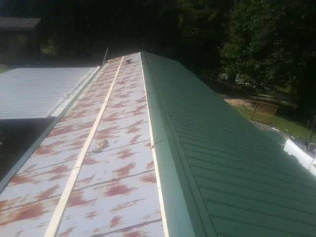Old rusted panels beside newly installed green metal roofing — Wind Damage Roof Repair by Roofing Brothers in Bradenville