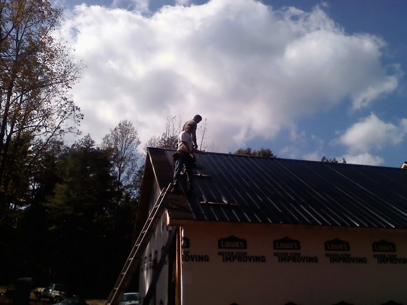 Roofer fastening dark metal panels high against a cloudy sky, from a Roof Inspection job in Bradenville