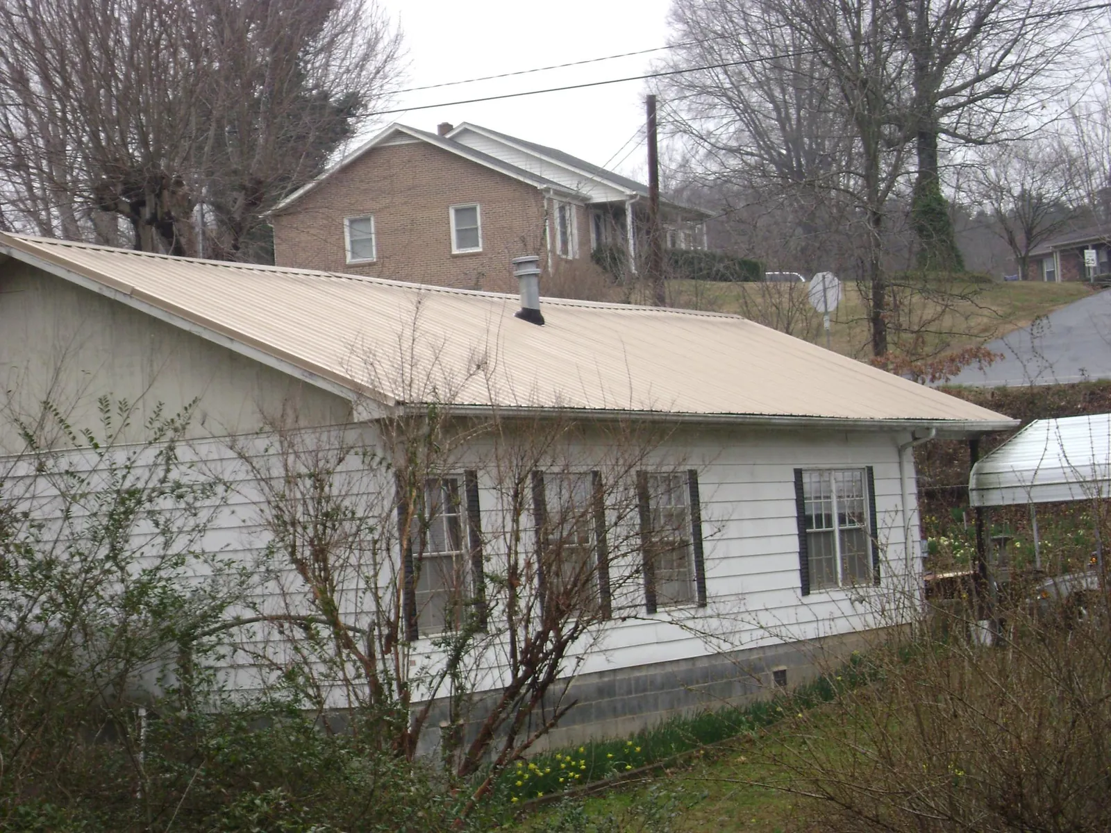 Tan metal roof on a white sided house set into a hillside — Commercial Roofing by Roofing Brothers in Bradenville